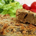 klaargemaakte vleesvervanger seitan met een korst van noten en kokos op een wit bord met een groen slaatje en tomaatjes