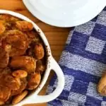 witte ovenschaal met deksel gevuld met vegetarische boboti met houten opscheplepel op keukenhanddoek